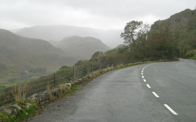 a very wet and windy road climbing a hill surrounded by misty hills in north wales